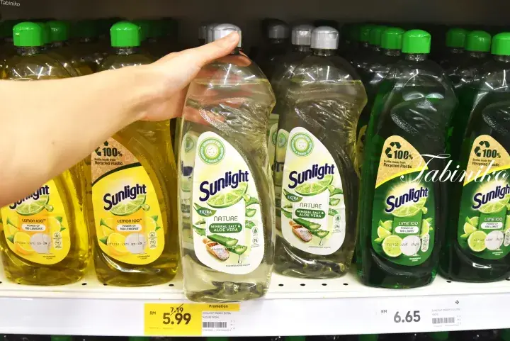 A hand selecting a bottle of Sunlight dishwashing liquid from a supermarket shelf with various scents.