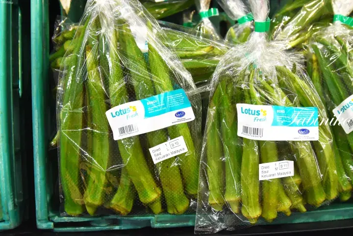 Fresh green okra packaged in clear plastic bags with Lotus’s Fresh labels at a Malaysian supermarket.