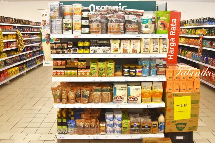 Well-stocked supermarket shelves displaying organic products and groceries with a ‘Harga Rata’ price sign in Malaysia.
