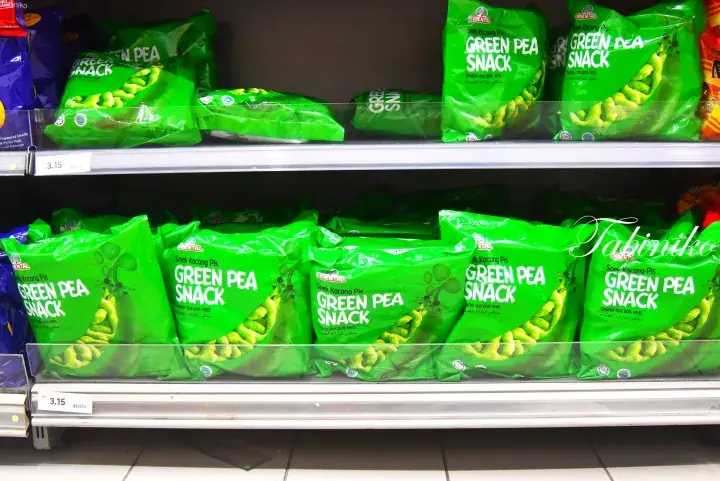 Shelves stocked with green bags of green pea snacks in a Malaysian grocery store aisle.