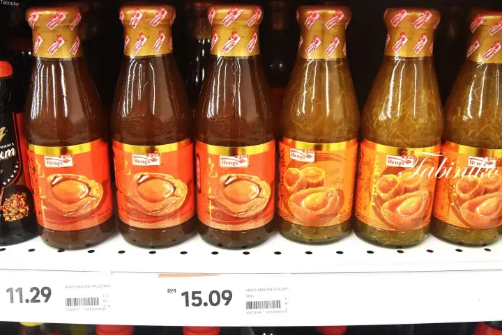 Rows of Heng’s abalone sauce bottles on a supermarket shelf with price tags showing RM 11.29 and RM 15.09.