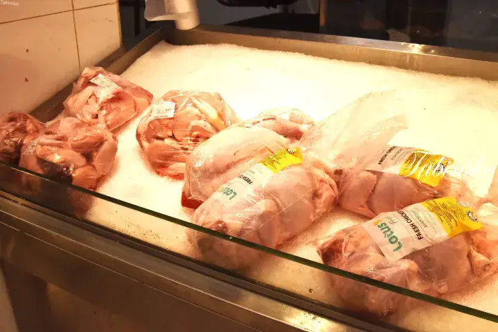 Fresh raw chicken pieces packaged in plastic bags and displayed on crushed ice in a refrigerated meat counter.