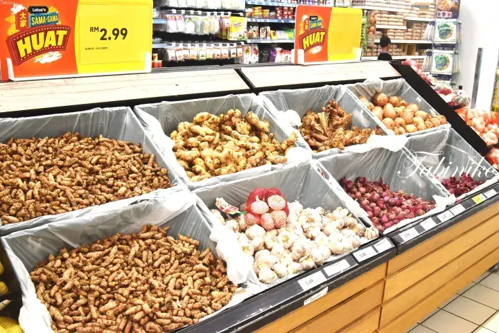 Fresh turmeric, ginger, garlic, shallots, and onions displayed in bins at a Lotte’s Huat promotion.