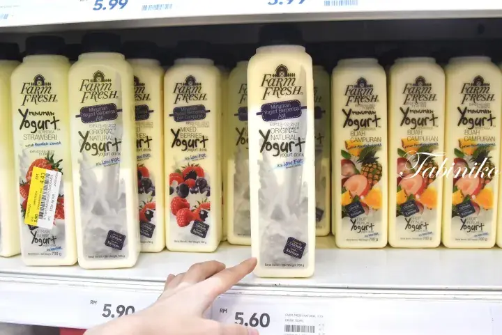 A hand points to a Farm Fresh Yogurt bottle on a supermarket shelf with price tags visible.