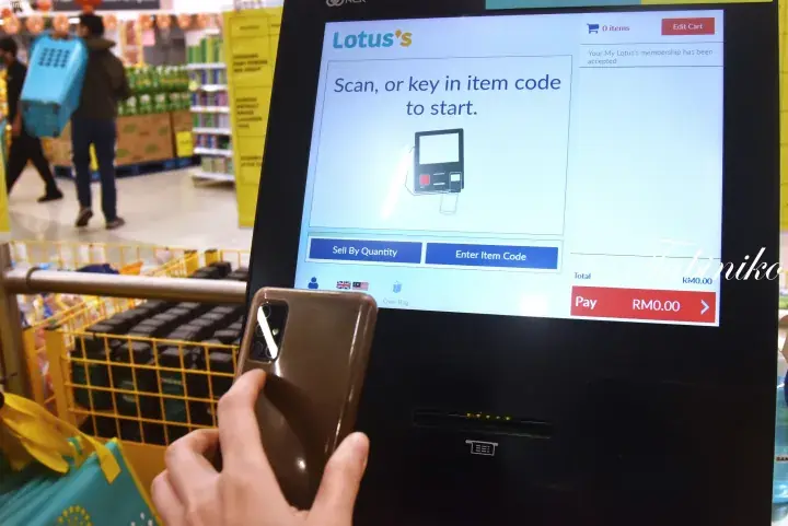 Customer scanning a product at a Lotus’s self-checkout kiosk in a Malaysian supermarket.