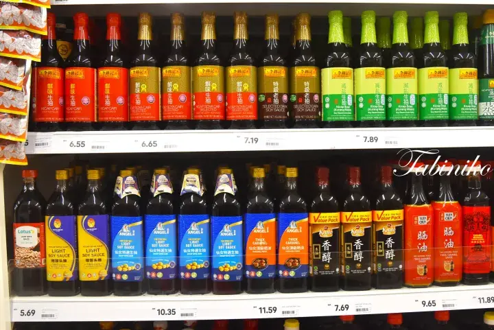 Shelves stocked with various soy sauce brands and bottles in a grocery store aisle.