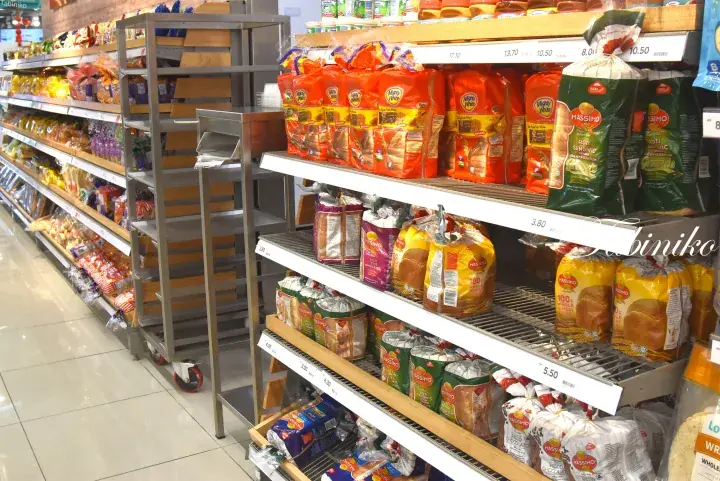 Well-stocked supermarket shelves displaying various packaged breads and snacks in a bright grocery store aisle.