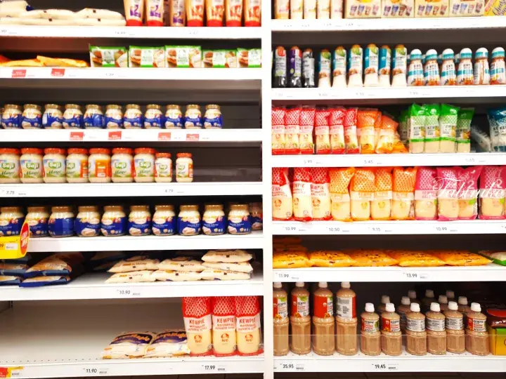 Well-stocked supermarket shelves displaying various condiments, sauces, and packaged food items.