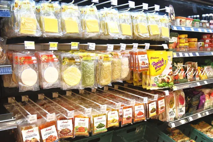 Shelves stocked with various packaged Indonesian food products including cheese, tortillas, and instant noodles in a Malaysian grocery store.