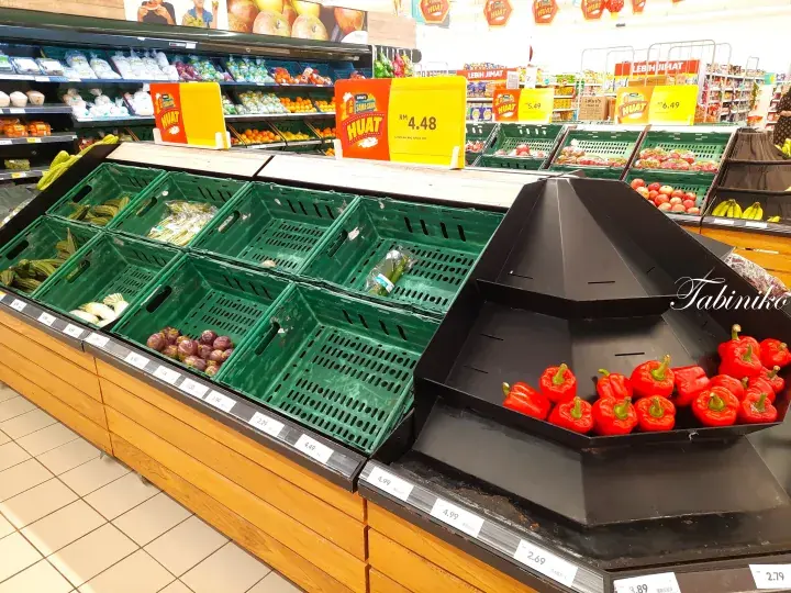 Empty green crates and red bell peppers on a supermarket shelf with promotional signs.