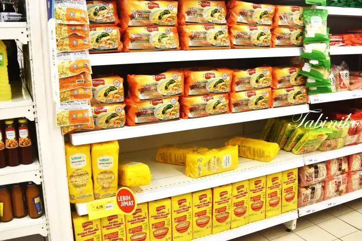 Shelves stocked with various instant noodles and snacks in a Malaysian grocery store aisle.