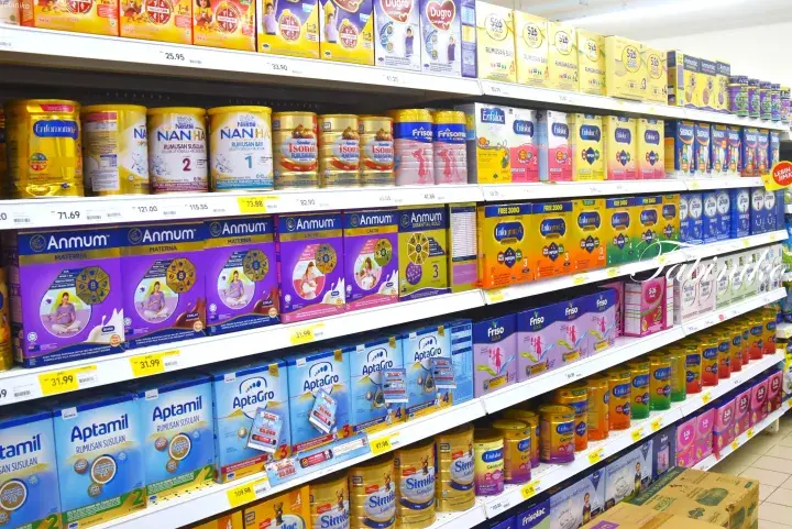 Shelves stocked with various baby formula brands like Anmum, Aptamil, and Friso in a Malaysian supermarket.