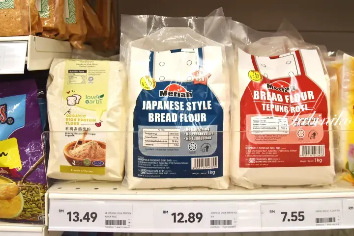 Shelves displaying various bread flour brands with price tags at a Malaysian supermarket.