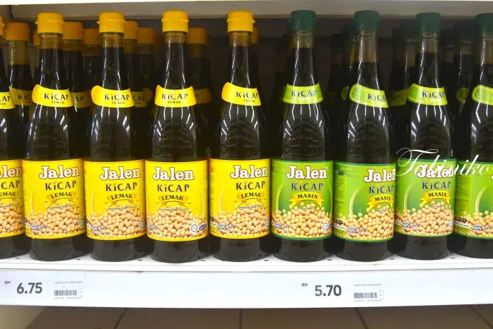Shelves of Jalen Kicap soy sauce bottles in yellow and green packaging displayed at a Malaysian supermarket.