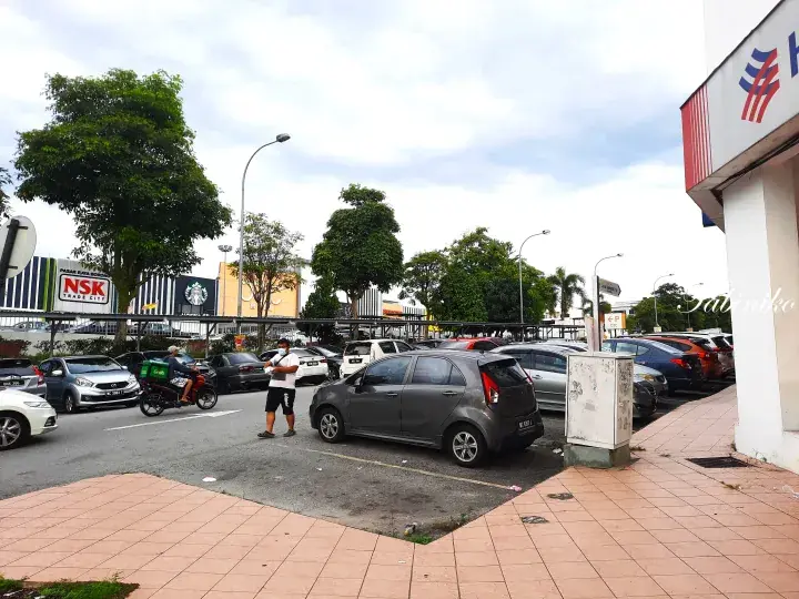 Parking lot with cars and a motorcyclist near NSK supermarket and Starbucks in Malaysia.