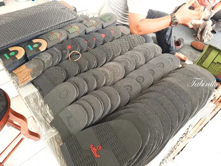 Rows of black rubber slippers and footwear soles displayed on a wooden table at a local market stall.