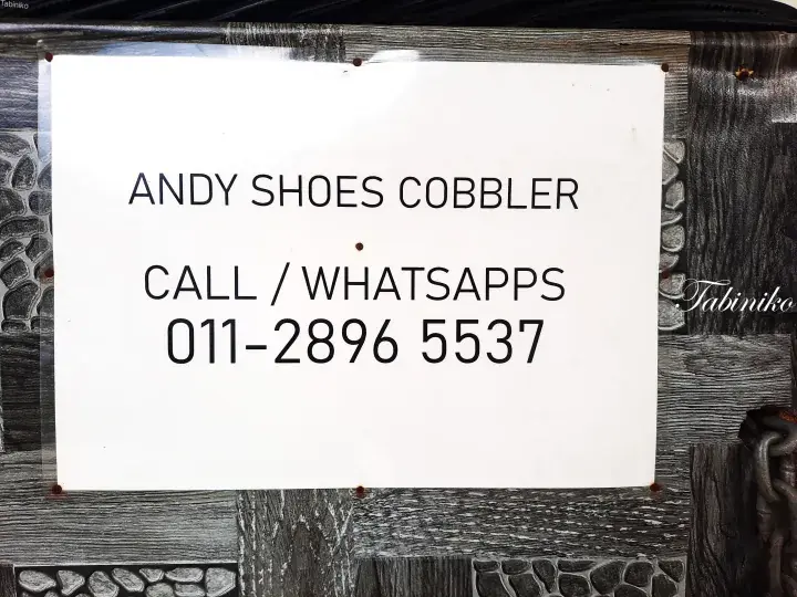 A white sign for Andy Shoes Cobbler with phone number 011-2896 5537 attached to a wooden surface.