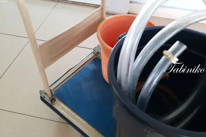 A blue utility trolley holding an orange bucket and a black bucket filled with clear plastic tubing.
