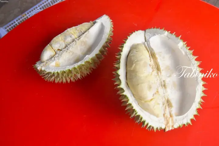 Fresh durian fruit split open on a bright red table, revealing creamy yellow flesh inside the spiky husk.