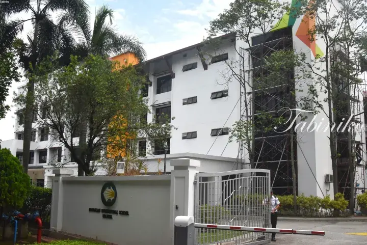 Exterior view of a white multi-story building with a gated entrance and a logo on the wall.