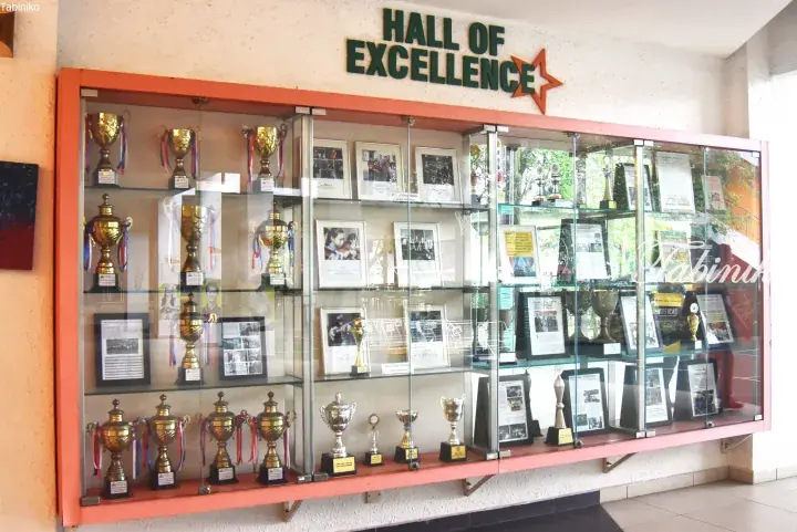 Glass display cabinet filled with trophies and framed certificates under a Hall of Excellence sign.