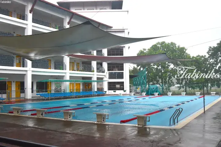 Outdoor swimming pool with starting blocks and shade sails at a residential building in Malaysia.