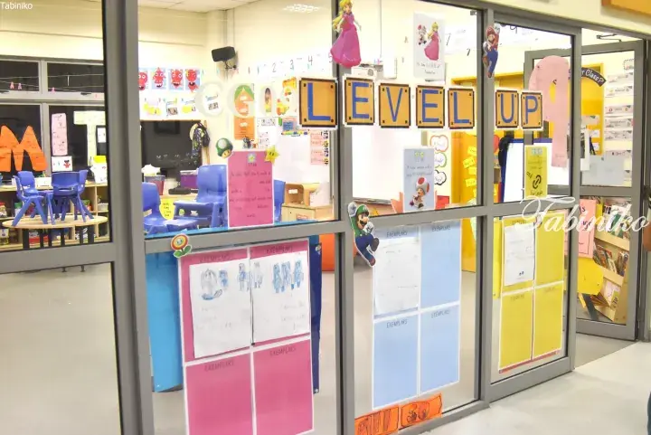 Glass classroom door decorated with colorful &lsquo;LEVEL UP&rsquo; letters and children&rsquo;s artwork.