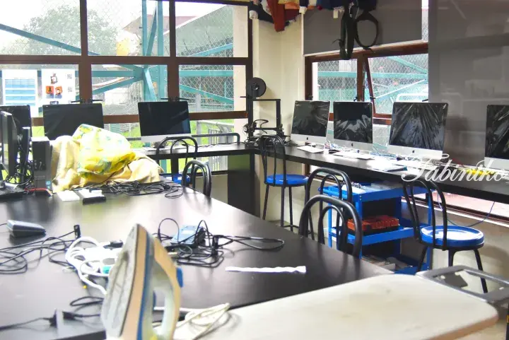 A computer lab with Apple monitors and a work table featuring an iron and cables.