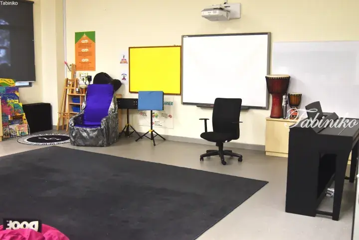 Spacious classroom featuring a purple armchair, whiteboard, projector, and musical instruments in a bright learning environment.