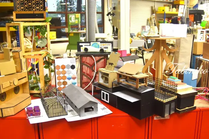 Architectural models and creative cardboard structures displayed on a red counter in a workshop setting.