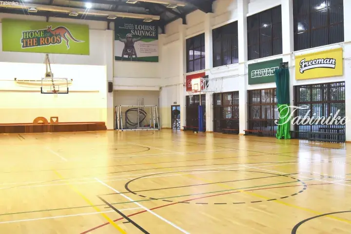 Spacious indoor basketball court with polished wooden flooring and banners including Home of the Roos and Louise Sauvage.