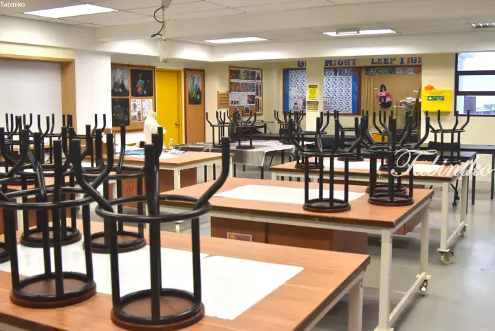 Classroom with wooden desks and black chairs stacked upside down for cleaning.
