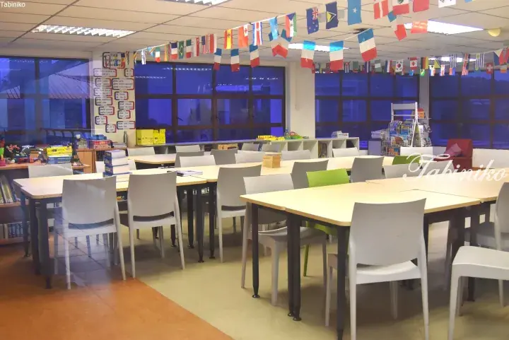 Bright classroom with tables, chairs, and international flags hanging from the ceiling.