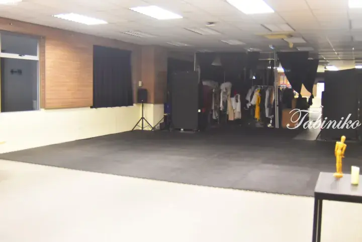 Interior of a dance studio with black flooring, mirrors, clothing racks, and a wooden mannequin on a table.