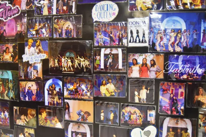 Wall display of musical theater posters and photos featuring titles like Dancing Queen and Donna and the Poppies.