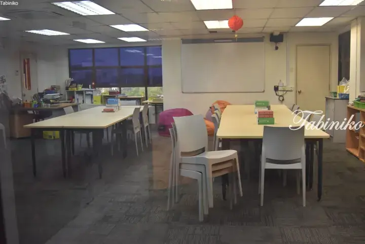 Bright study room with long tables, chairs, and a whiteboard, featuring a red lantern and books.