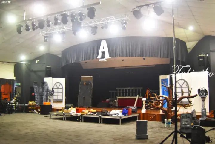 Stage setup for a theatrical production featuring a large letter A backdrop, props, and lighting rig in a performance hall.