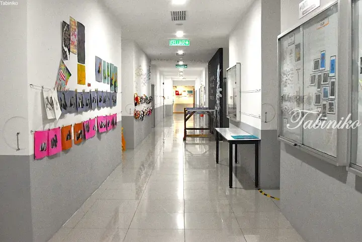 Bright hallway with student artwork on display and a green exit sign at INTI International University.