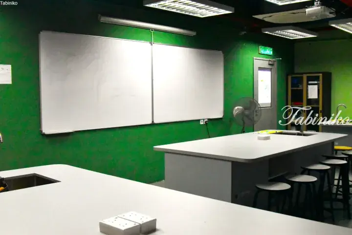 Modern kitchen with white countertops, green walls, and a large whiteboard, likely a cooking class or rental space.
