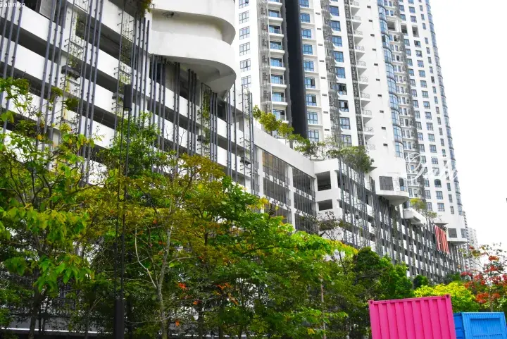 Modern white high-rise building with curved balconies and vertical greenery, surrounded by lush trees and colorful shipping containers.