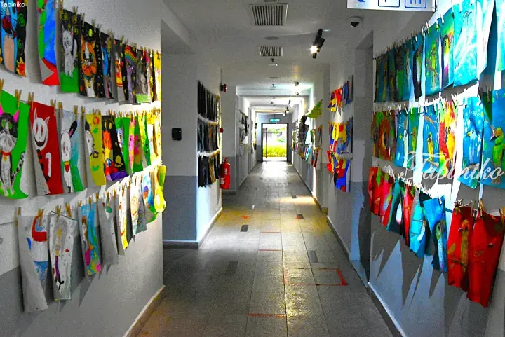 Colorful children&rsquo;s artwork displayed on strings in a bright school hallway.