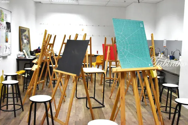 Wooden easels with black and green boards in a bright art studio classroom with stools and sinks.
