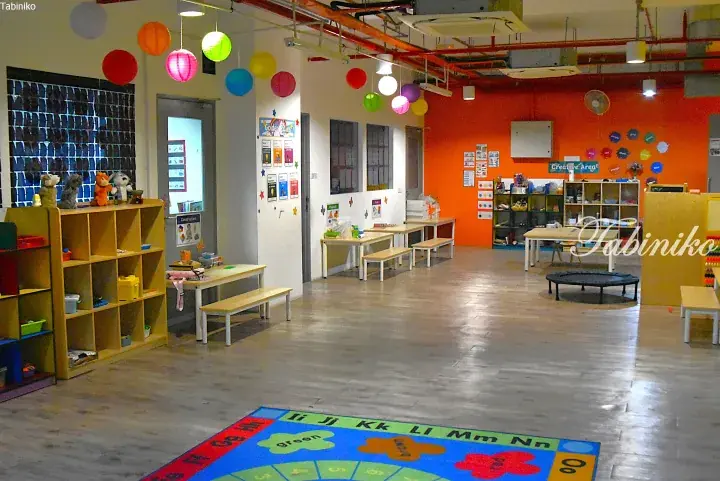 Colorful kindergarten classroom with wooden shelves, tables, and a letter rug in a modern space.