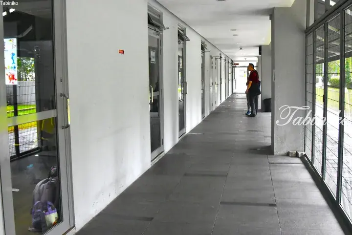 Long corridor with glass doors and metal grilles at a modern building, with two people standing near the end.