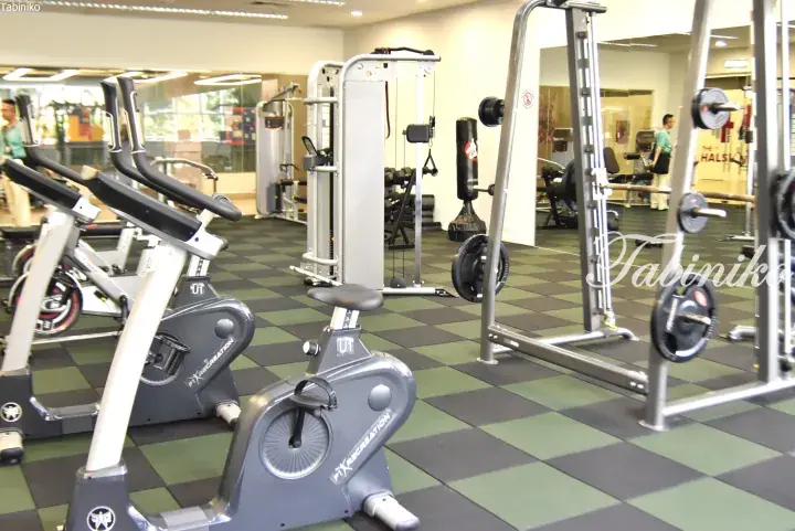 Fitness equipment including stationary bikes and weight machines in a modern gym with green and black flooring.