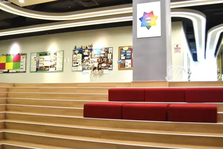 Modern tiered wooden seating area with red cushions and bulletin boards in a bright interior space.