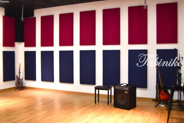 Music studio with red and blue acoustic panels, guitars, and amplifier on wooden floor.