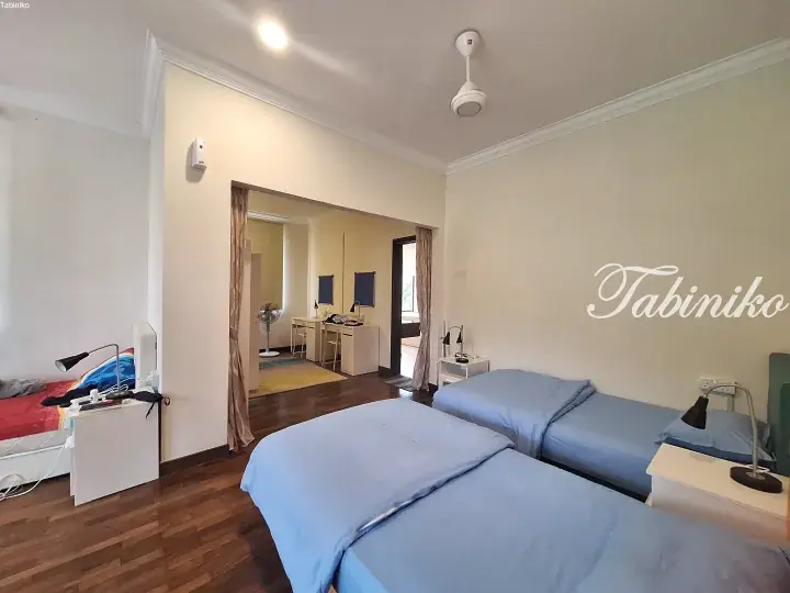 Bright dormitory room with twin beds, wooden floors, and a shared study area visible through an open doorway.