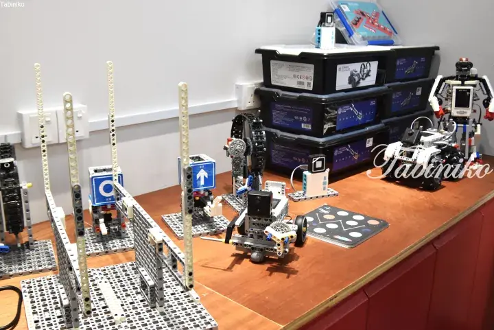LEGO robotics kits and educational models displayed on a wooden table with storage boxes in the background.