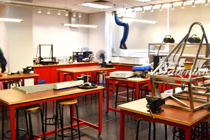 Modern workshop with red tables, 3D printers, and metal frames in a bright creative space.